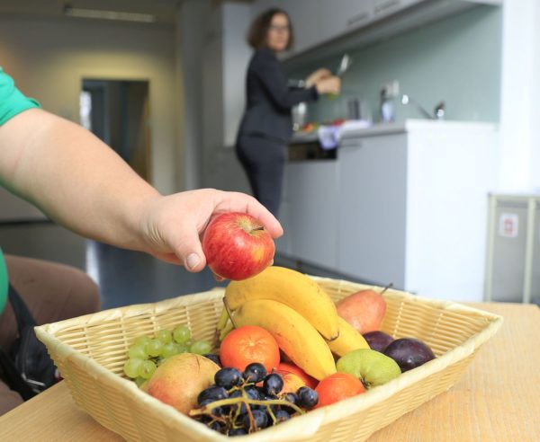 Eine Hand greif sich was aus dem Obstkorb. Eine Frau schaut zu.