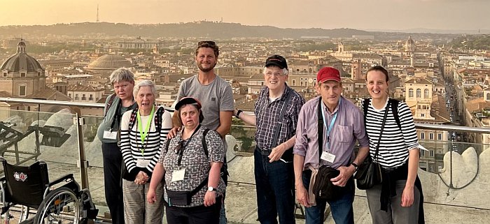Fünf Menschen mit Behinderungen stehen auf einer Aussichtsplattform über einer Stadt mit Kirchen und Kuppeln (Rom).