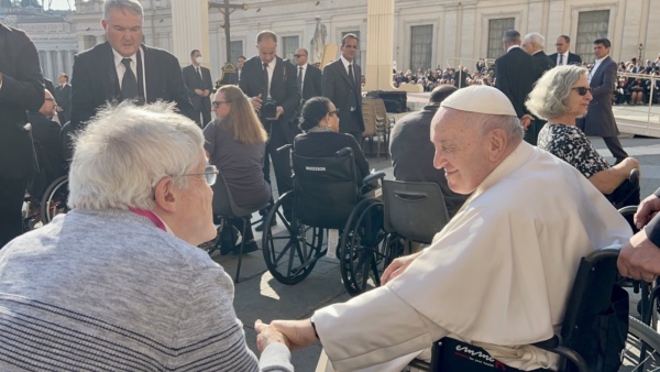 Ein Mann im Rollstuhlfahrer schüttelt Papst Franziskus die Hand.