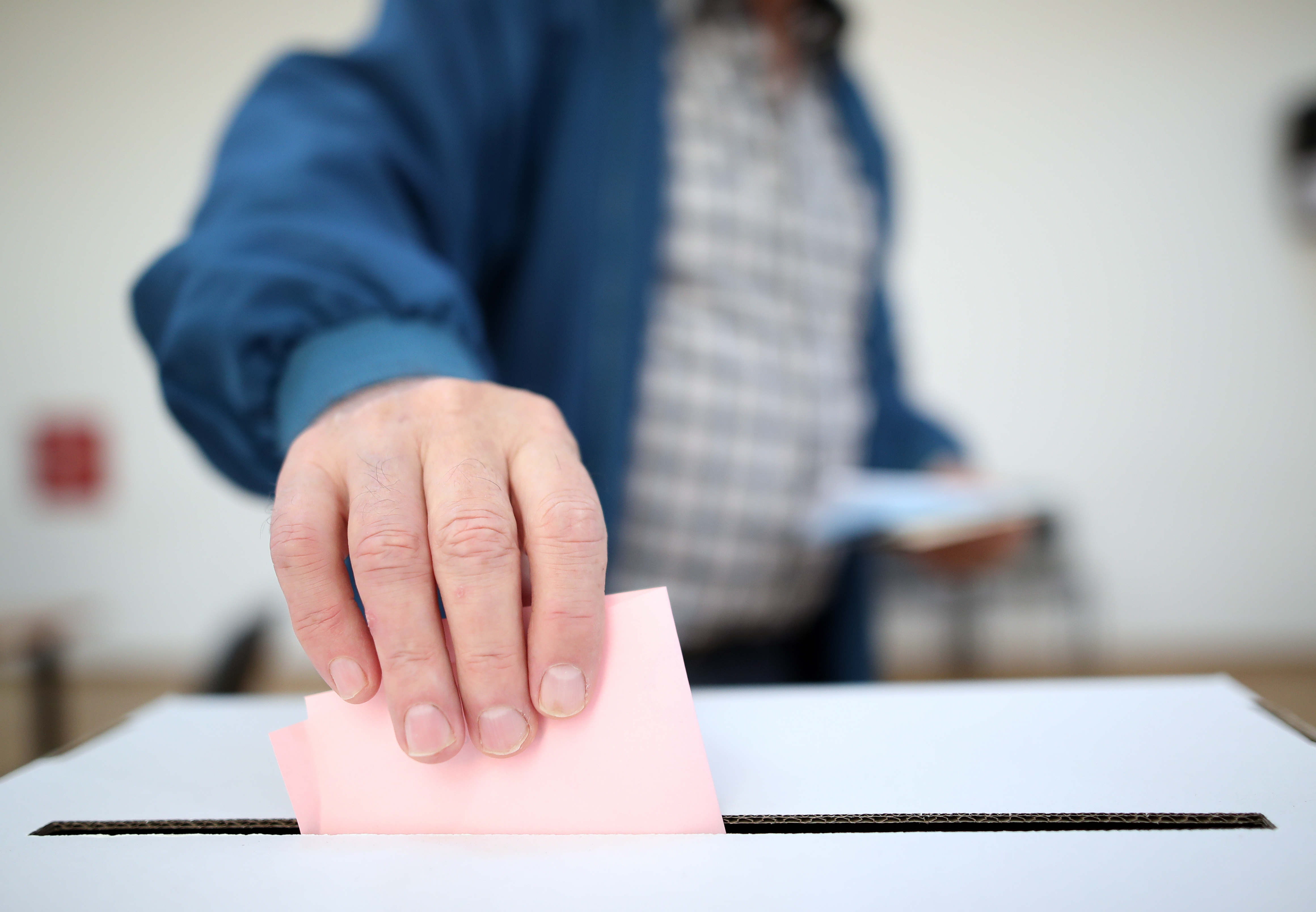 Eine Männer-Hand wirft einen Stimmzettel in eine Wahlurne.