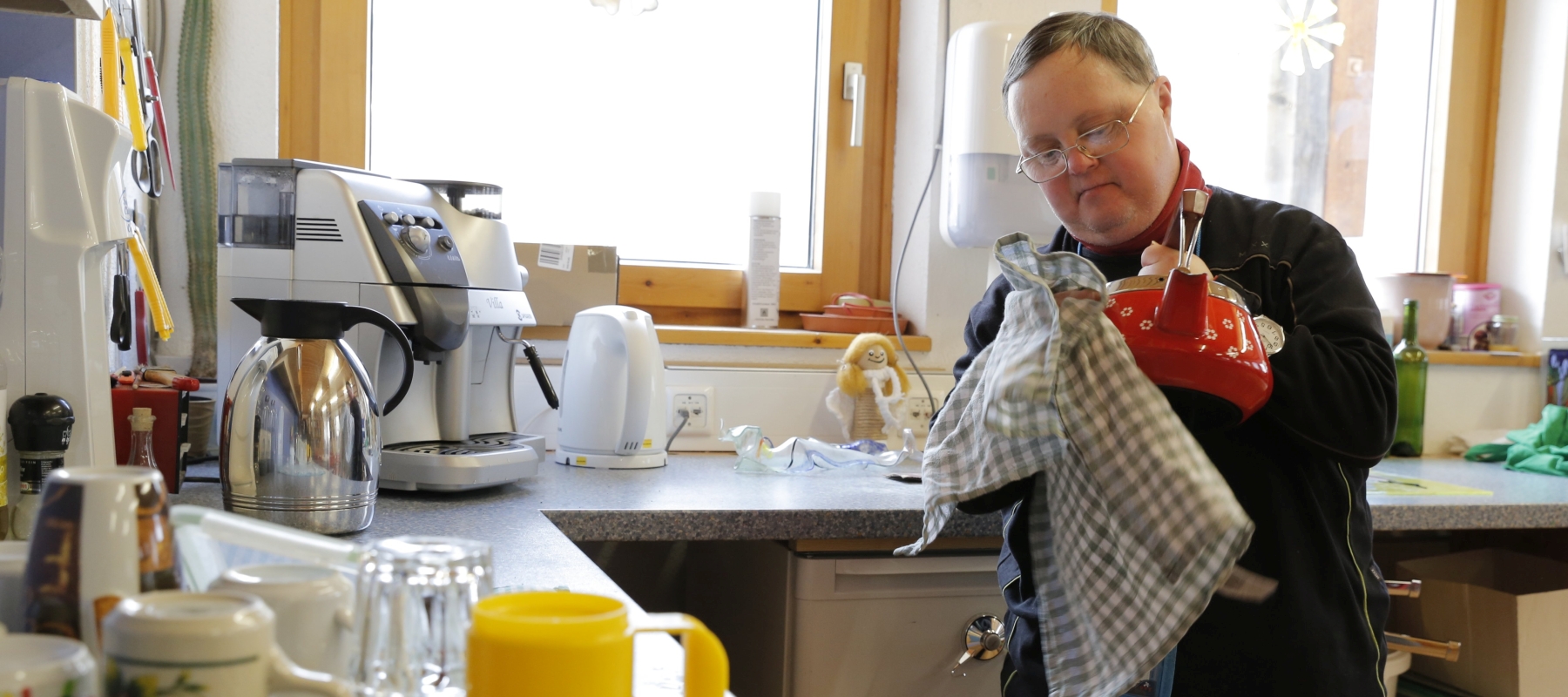 Ein Mann mit Down-Syndrom steht in der Küche und trocknet eine Teekanne ab.