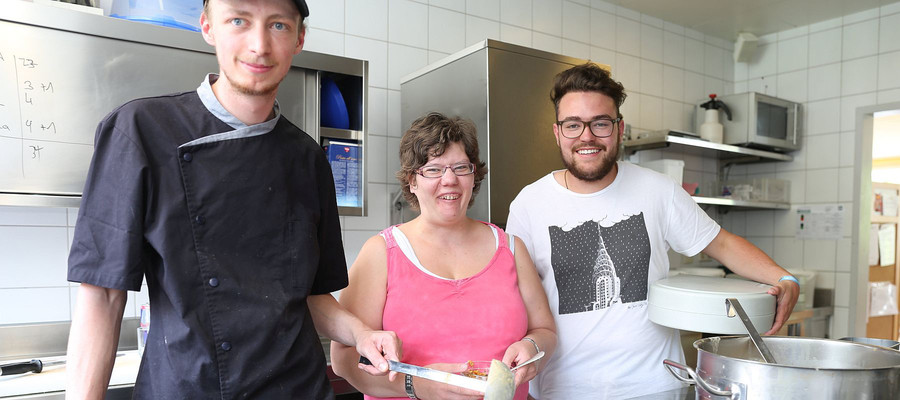 Zwei junge Köche und eine Frau stehen in einer Küche